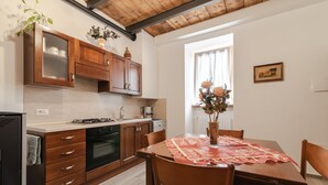 A kitchen with wooden cabinets, a dining table with a red tablecloth, and a window with curtains. - Holiday Home 'Casa Pifaro' in Monterchi (Monterchi)
