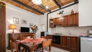 A modern kitchen with wooden cabinets, a dining table with chairs, a TV, and a vase with flowers. - Holiday Home 'Casa Pifaro' in Monterchi (Monterchi)
