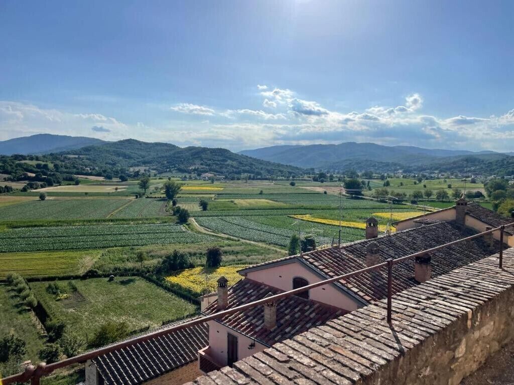 A view from a building's terrace overlooking a rural landscape with fields and distant hills.