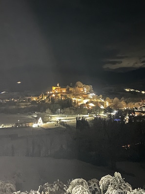 Vista nocturna de un edificio histórico con ventanas iluminadas y una torre destacada, rodeado por un paisaje montañoso.