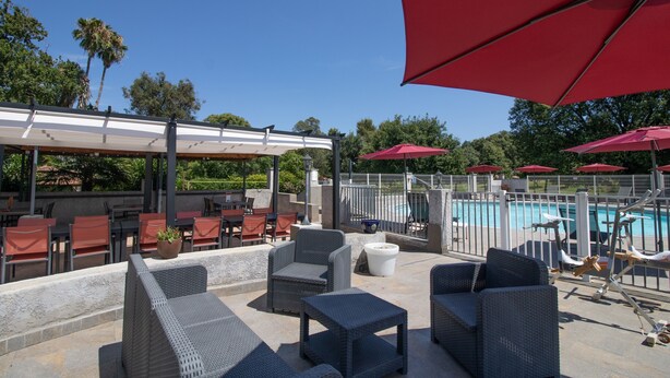 Zona de terrassa a l'aire lliure amb mobles de vimet, ombrelles vermelles i una piscina.