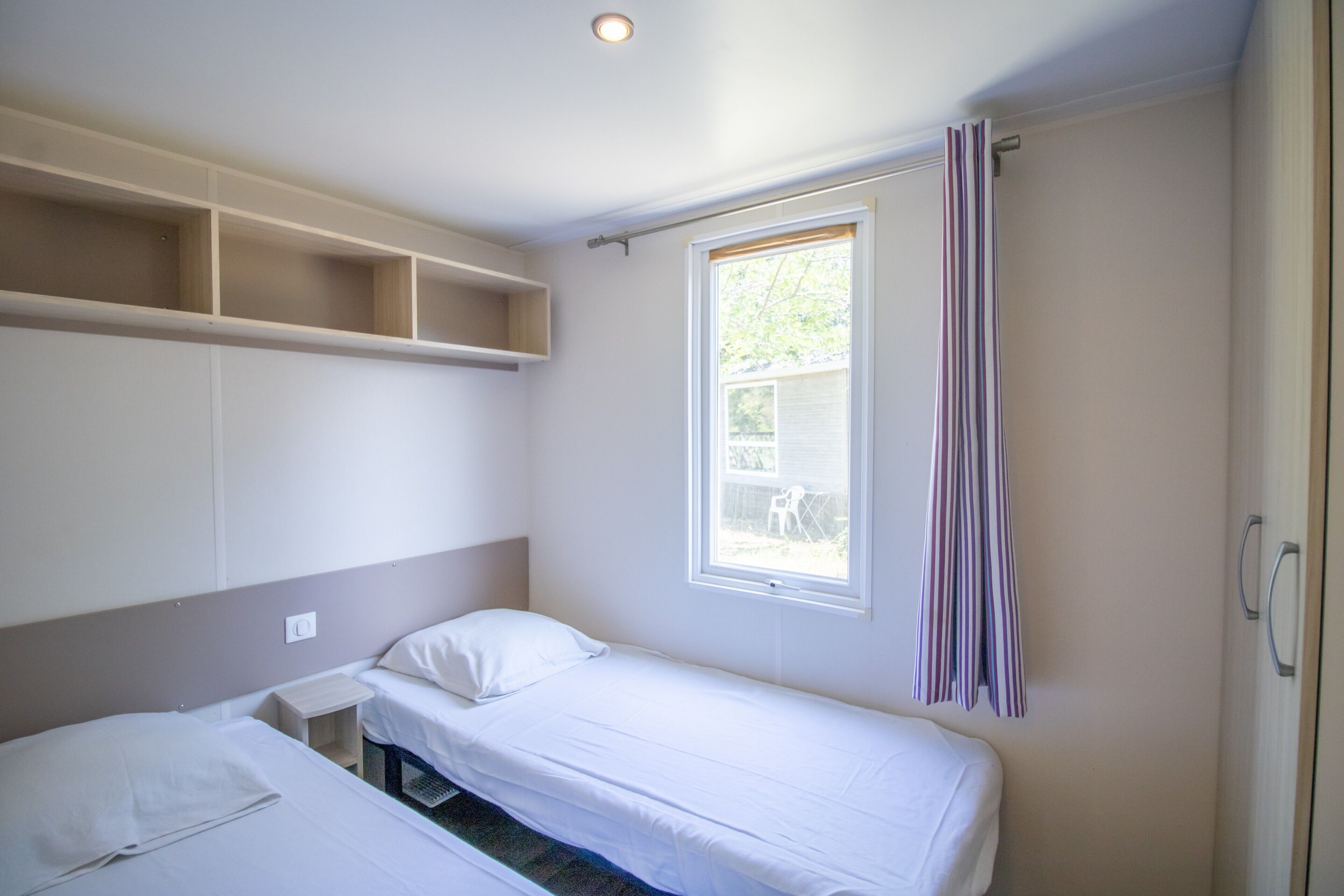 Une petite chambre avec un lit simple, une fenêtre, une étagère et une armoire.