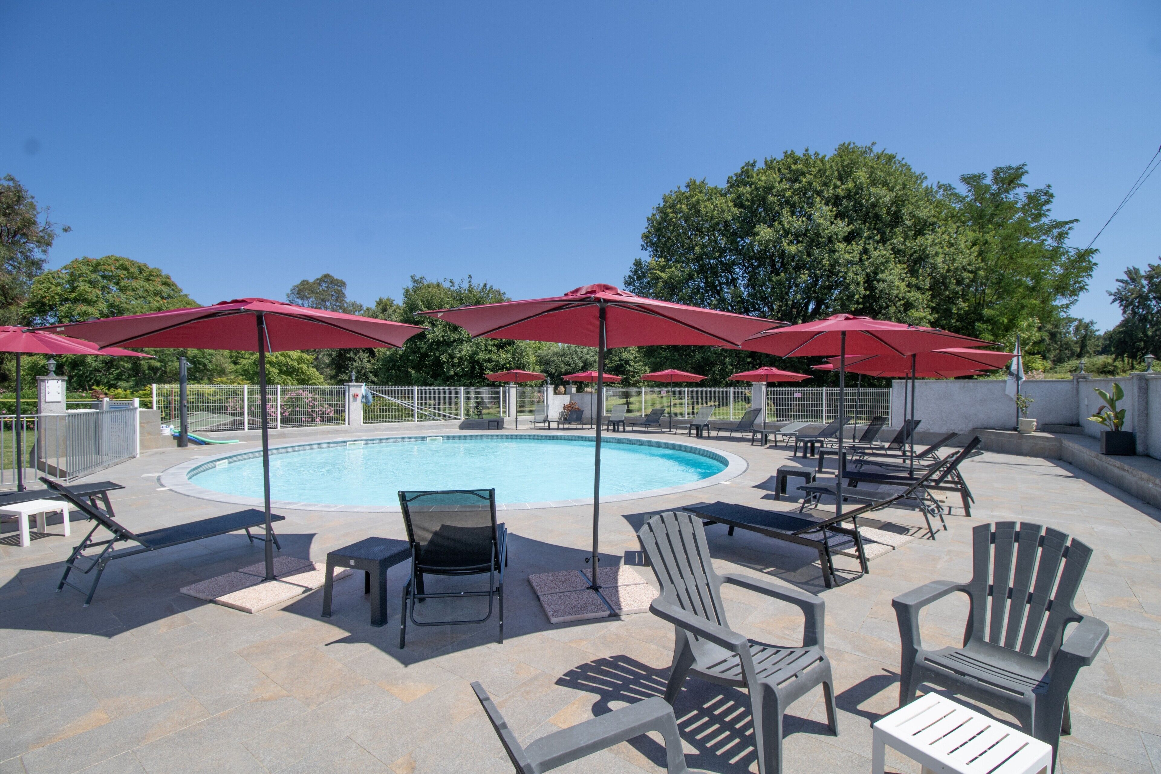 Un espace aménagé au bord de la piscine, avec des chaises longues, des parasols rouges et un ciel d’un bleu limpide.