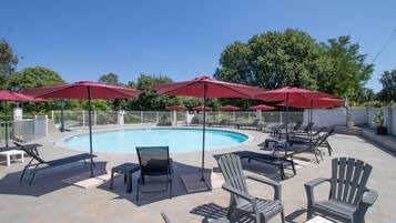 Un espace aménagé au bord de la piscine, avec des chaises longues, des parasols rouges et un ciel d’un bleu limpide.