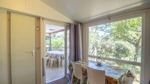 A room with a table and chairs, a door leading to an outdoor area, and a window with a view of greenery. - 2ème mobilhome tout confort (Taglio-Isolaccio)