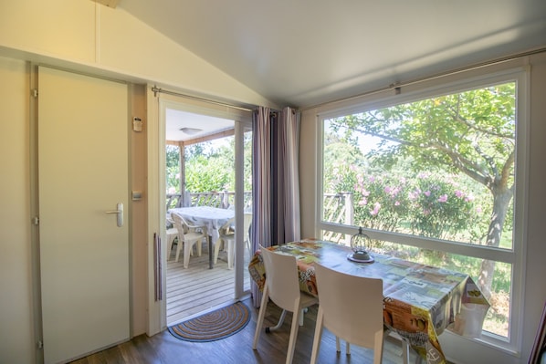 Ein Zimmer mit Tisch und Stühlen, einer Tür zu einem Außenbereich und einem Fenster mit Blick auf Grünflächen.