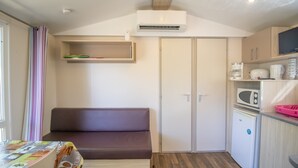 A compact kitchenette with a microwave, coffee maker, and refrigerator. A brown sofa is positioned near a window with a striped curtain. - 2ème mobilhome tout confort (Taglio-Isolaccio)