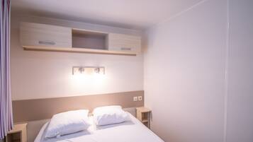 A hotel room with a bed, bedside tables, a light fixture above the bed, and a wall-mounted shelf.