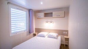 A bedroom with a bed, bedside tables, a window with blinds, and built-in shelving. - 2ème mobilhome tout confort (Taglio-Isolaccio)