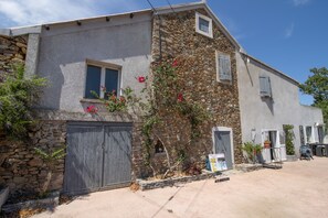 Ein zweistöckiges Gebäude mit einer Stein-Fassade, einer Holztür zur Garage und einem kleinen Fenster mit Rollläden.