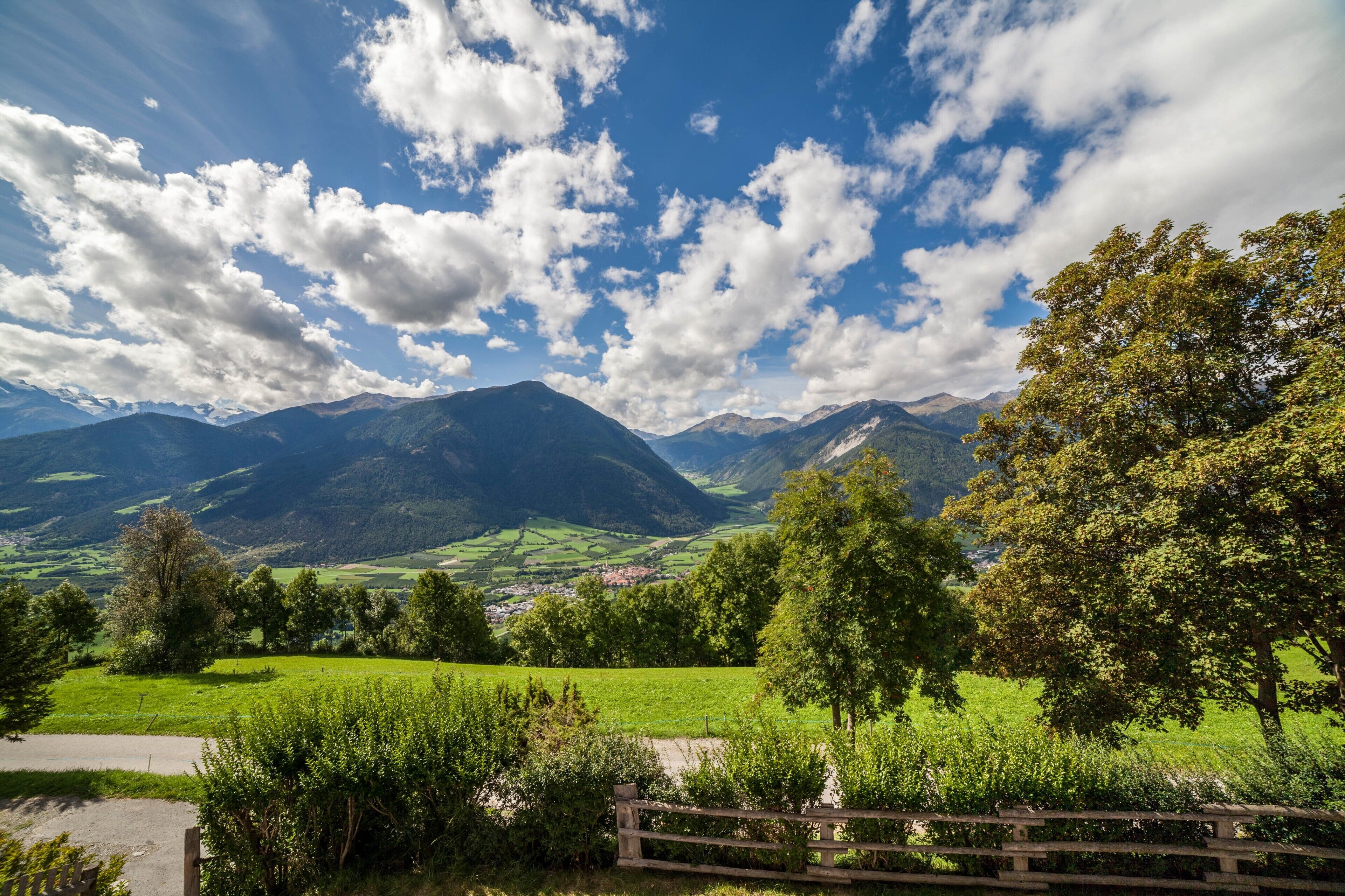 Eine gebirgige Landschaft mit blauem Himmel, grünen Feldern und einem Holzzaun.