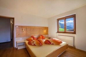 A bedroom with a wooden headboard, a bed with orange pillows, a window with a mountain view, and a radiator.