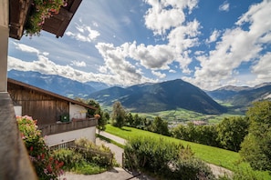 A mountain view from a building with a balcony, a wooden fence, and a pathway leading to the entrance.