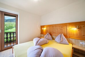 A bedroom with a wooden headboard, a bed with pillows, a nightstand, and a view of a green landscape through a glass door.