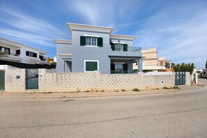 A modern two-story house with a balcony, a stone wall, and a clear sky.