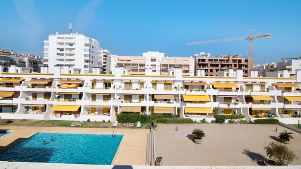 Un hotel con varios balcones, piscina y una grúa de construcción al fondo.