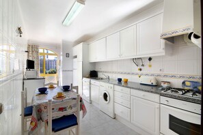 A kitchen with white cabinets, a washing machine, a gas stove, and a dining area with a table and chairs.