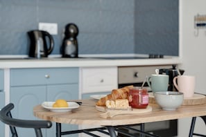 A breakfast table with croissants, a plate of fruit, a jar of jam, and a bowl.