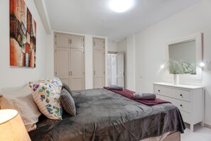 Une chambre à coucher avec un lit, une commode, un miroir et un tableau accroché au mur.