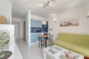 Un espace de vie compact comprenant un coin cuisine, un espace repas et un canapé vert.