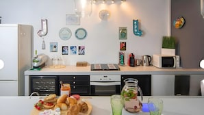 Een moderne keuken met een magnetron, waterkoker en diverse keukenapparaten. Er zijn decoratieve wandpanelen en een houten snijplank met etenswaren.