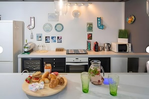 A modern kitchen with a microwave, kettle, and various kitchen appliances. There are wall decorations and a wooden cutting board with food items.