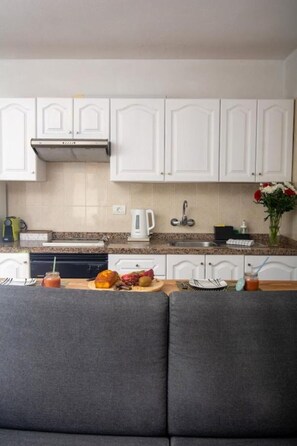 A kitchen with white cabinets, a stove, a coffee maker, and a dining area with a grey sofa.