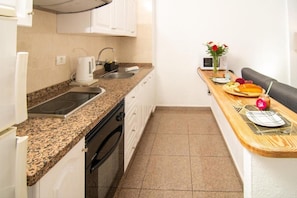 A compact kitchen with a granite countertop, a built-in oven, a sink, and a wooden dining table with a vase of flowers.