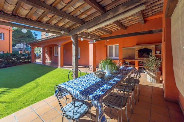 An outdoor patio with a table and chairs, a brick oven, and a well-maintained lawn.