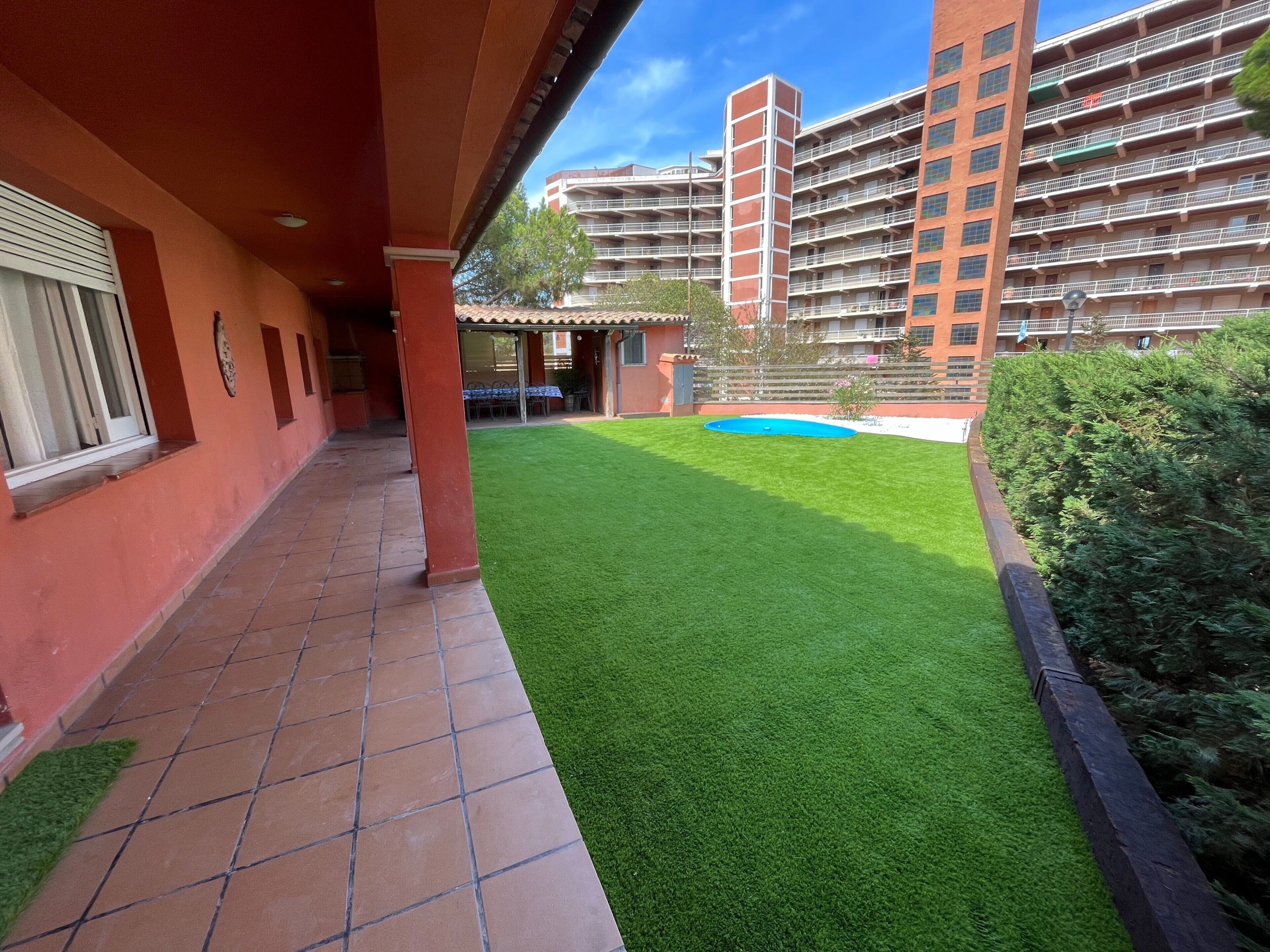 Une cour avec une pelouse artificielle, une petite piscine et un bâtiment doté de plusieurs balcons.