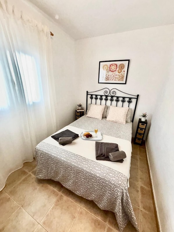 A neatly made bed with a patterned bedspread, pillows, and a small plate of fruit on the bedside table.