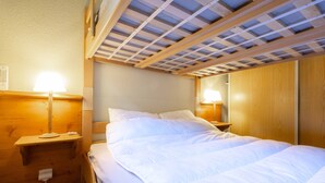 Ein Zimmer mit einem Bett, einem Holzkopfteil, zwei Nachttischlampen, einem Nachttisch aus Holz und einer Decke mit Holzbalken.