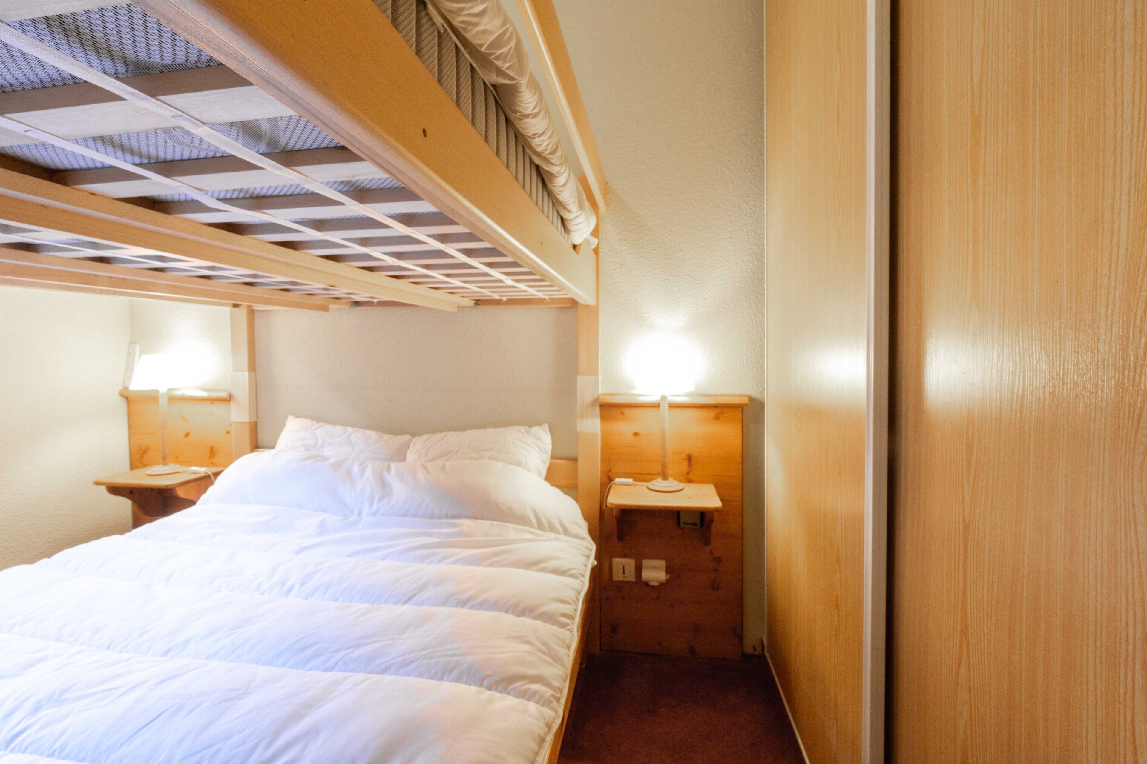 A single bed with a headboard, two bedside tables with lamps, a wooden wardrobe, and a sloped ceiling with a grid pattern.