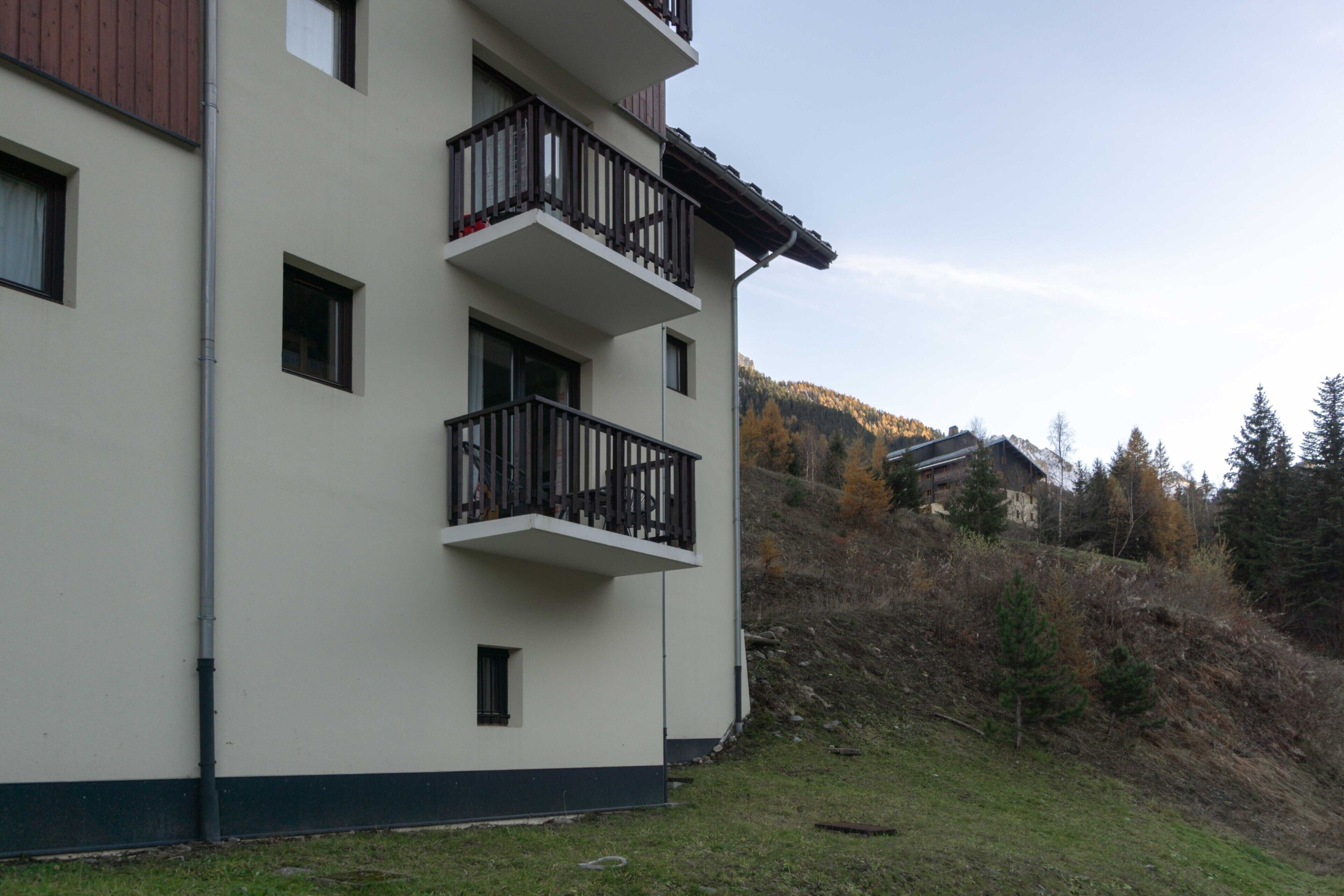En byggnad med flera våningar och balkonger, ett grönområde framför och ett kuperat landskap i bakgrunden.