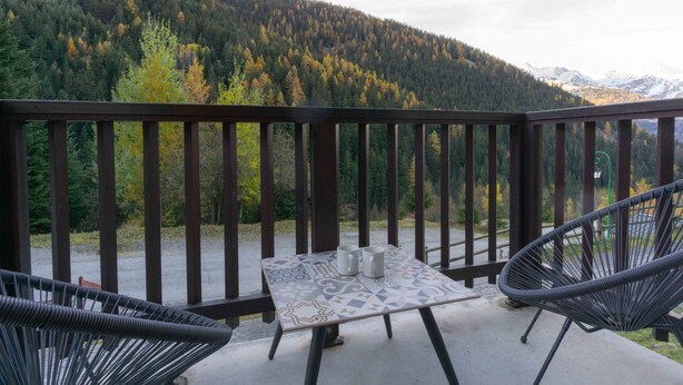 Ein Balkon mit Tisch und Stühlen mit Blick auf einen bewaldeten Berg.