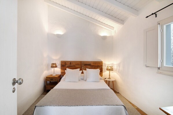 Une chambre à coucher avec une tête de lit en bois, deux tables de chevet avec des lampes, un lit avec une literie blanche et une fenêtre donnant sur un paysage agréable.