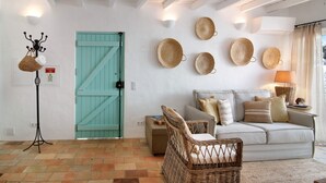 Una habitación con una puerta verde azulado, muebles de mimbre, un sofá blanco y cestas fijadas a la pared.