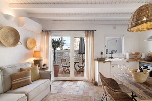 A cozy living area with a sofa, a dining table, wicker chairs, a kitchen area, and a sliding glass door leading to an outdoor patio. - Holiday Home 'Casa De Benafim 51' with Shared Pool, Shared Garden & Wi-Fi (Benafim)