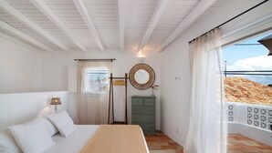 Un dormitorio con cama, cómoda, espejo y ventana con vista a un edificio.