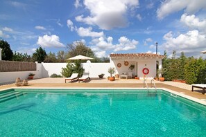 A clear swimming pool with a white building in the background, a wooden deck, and a clear sky.