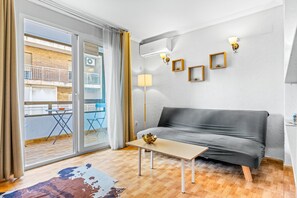 Un salon moderne avec un canapé, une petite table et une lampe sur pied. Une porte-fenêtre coulissante donne accès à un balcon.