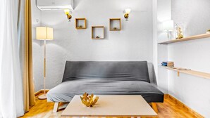 Een moderne woonkamer met een grijze bank, een houten salontafel en een decoratieve schaal. Er zijn wandlampen en een plank met boeken.