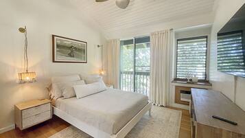 A bedroom with a bed, bedside lamps, a ceiling fan, a window with curtains, and a small table with a vase.
