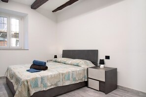 Un dormitorio con cama, mesita de noche, lámpara y ventana.