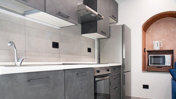 Una cocina moderna con armarios grises, un refrigerador de acero inoxidable, un horno empotrado y un microondas sobre una repisa de madera.