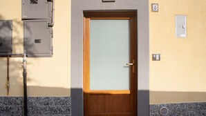 Una puerta con un panel de vidrio esmerilado, un picaporte de metal y un buzón pequeño en la pared.