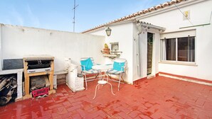 Un patio con suelo de ladrillo rojo, una mesita con dos sillas, un estufa de leña y una ventana.