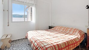Un dormitorio con cama, ventana, mesita de noche y mesilla.
