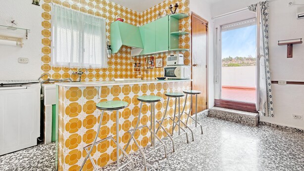 Una cocina con pared decorada, una ventana con cortinas, un mueble verde y una puerta que da al exterior.
