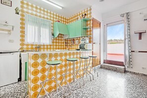 Eine Küche mit einer Wand mit Muster, einem Fenster mit Vorhängen, einem grünen Schrank und einer Tür, die nach draußen führt.